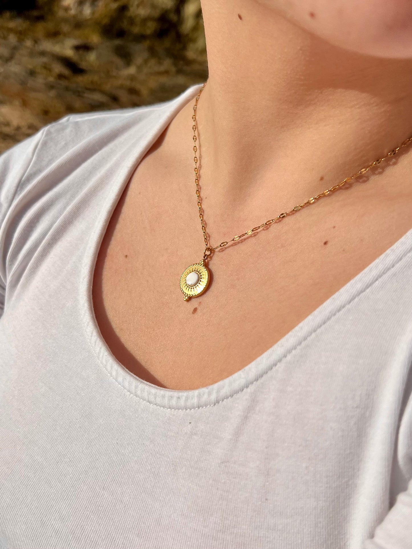 Collier ZÉLIE en acier inoxydable doré et pierre de Howlite, porté par une fille dans des rochers.