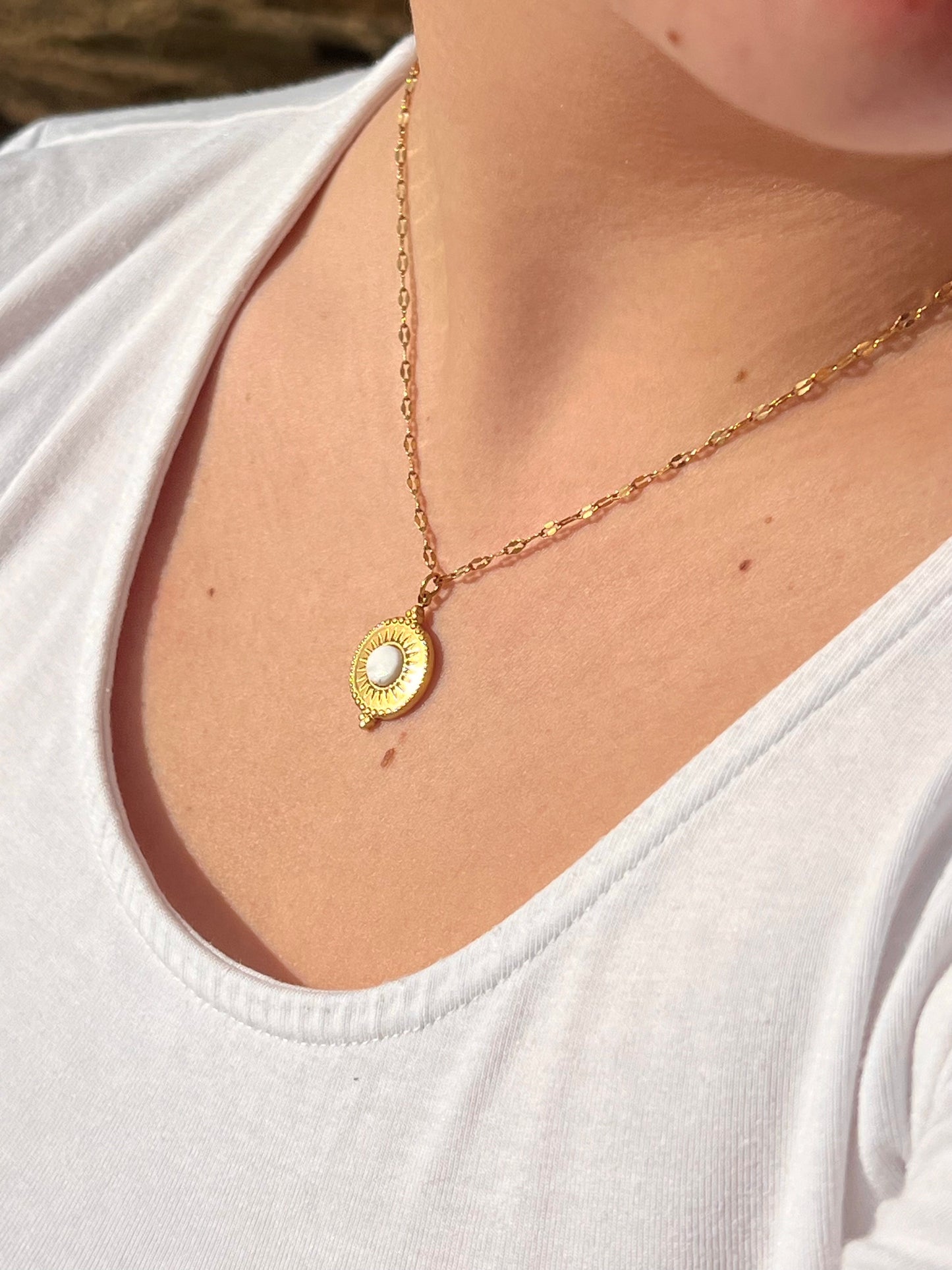 Collier ZÉLIE en acier inoxydable doré et pierre de Howlite, porté par une fille dans des rochers.