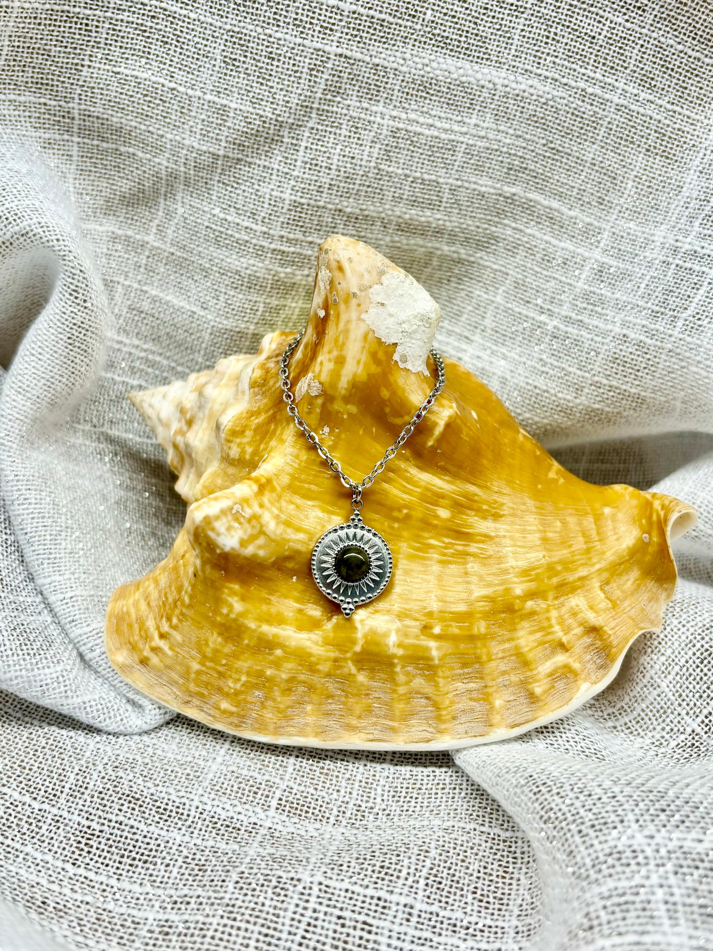 Collier ZÉLIE en acier inoxydable argent et pierre de Labradorite, exposé sur un coquillage et un fond en lin.
