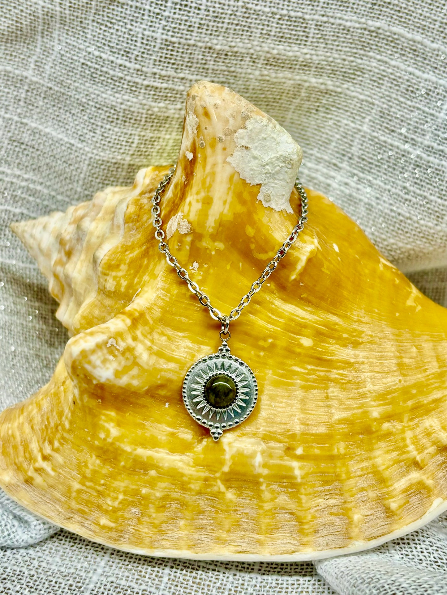 Collier ZÉLIE en acier inoxydable argent et pierre de Labradorite, exposé sur un coquillage et un fond en lin.