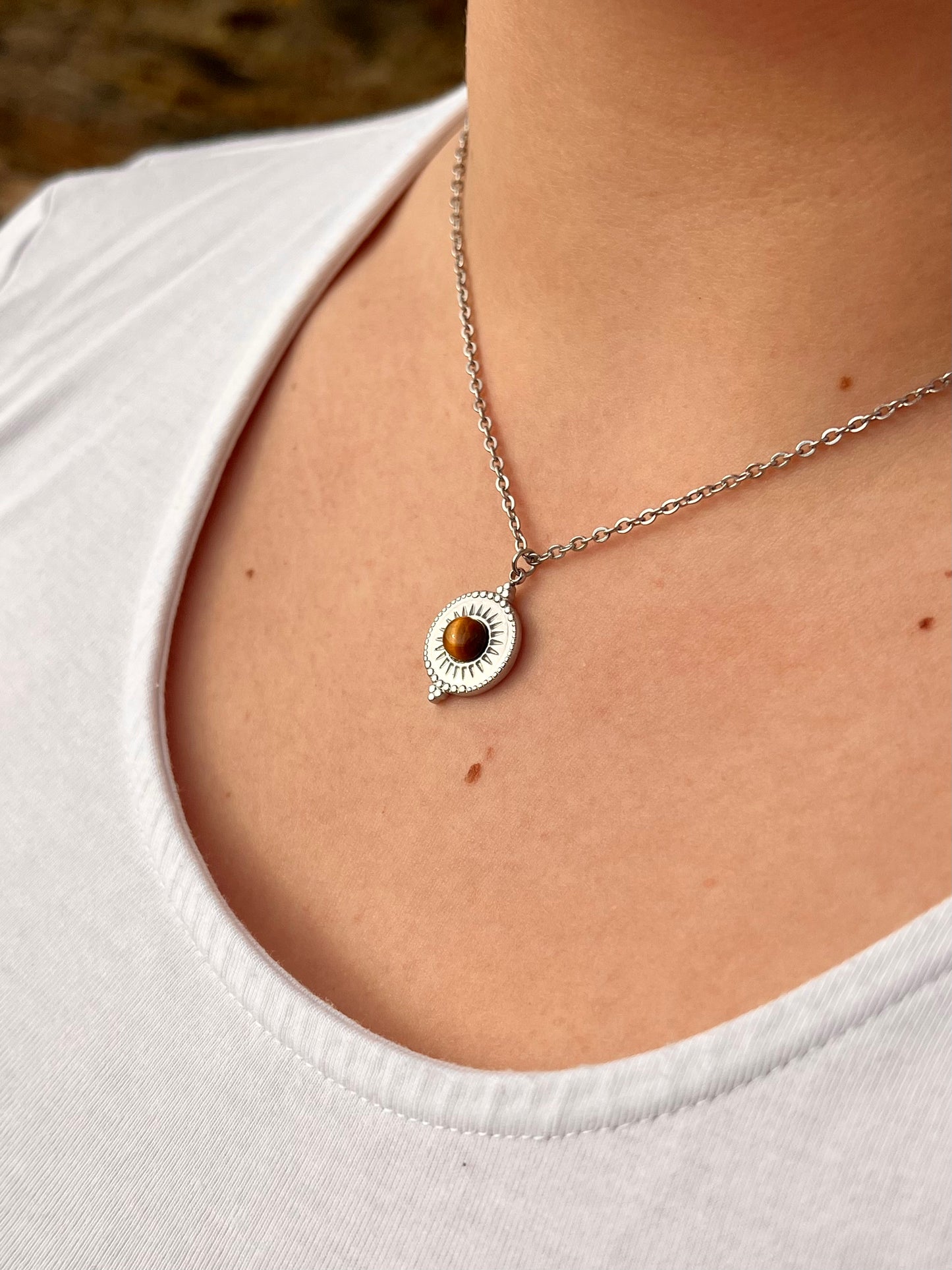 Collier ZÉLIE en acier inoxydable argent et pierre d'oeil de tigre, porté par une fille dans les rochers