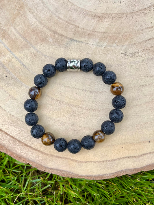 Bracelet ADAM, avec Pierre de Lave et Oeil de Tigre, exposé sur un rondin de bois.