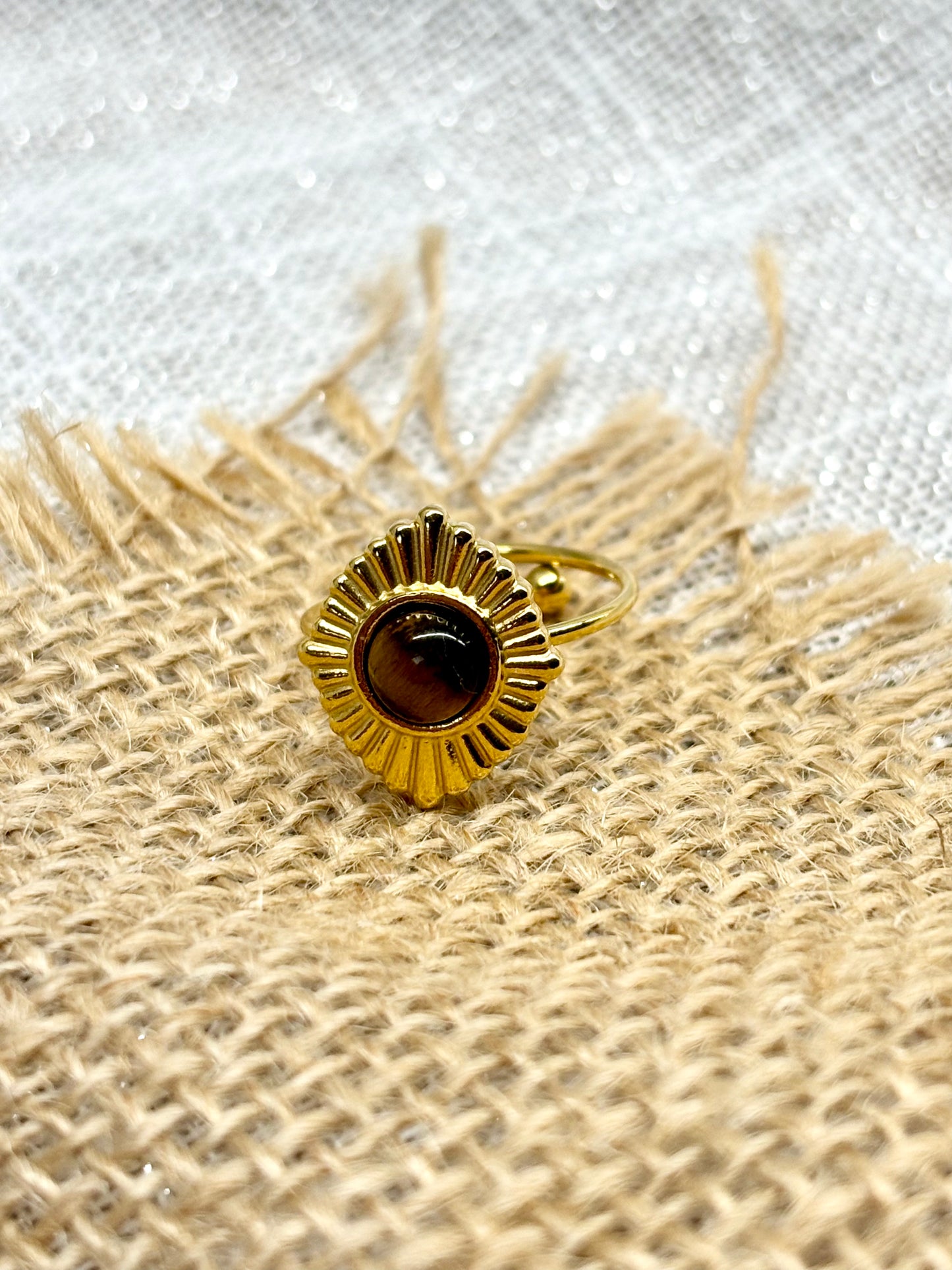 Bague ALYSÉE, de couleur dorée avec pierre d'Oeil de Tigre, exposée sur un fond en lin et toile de jute.