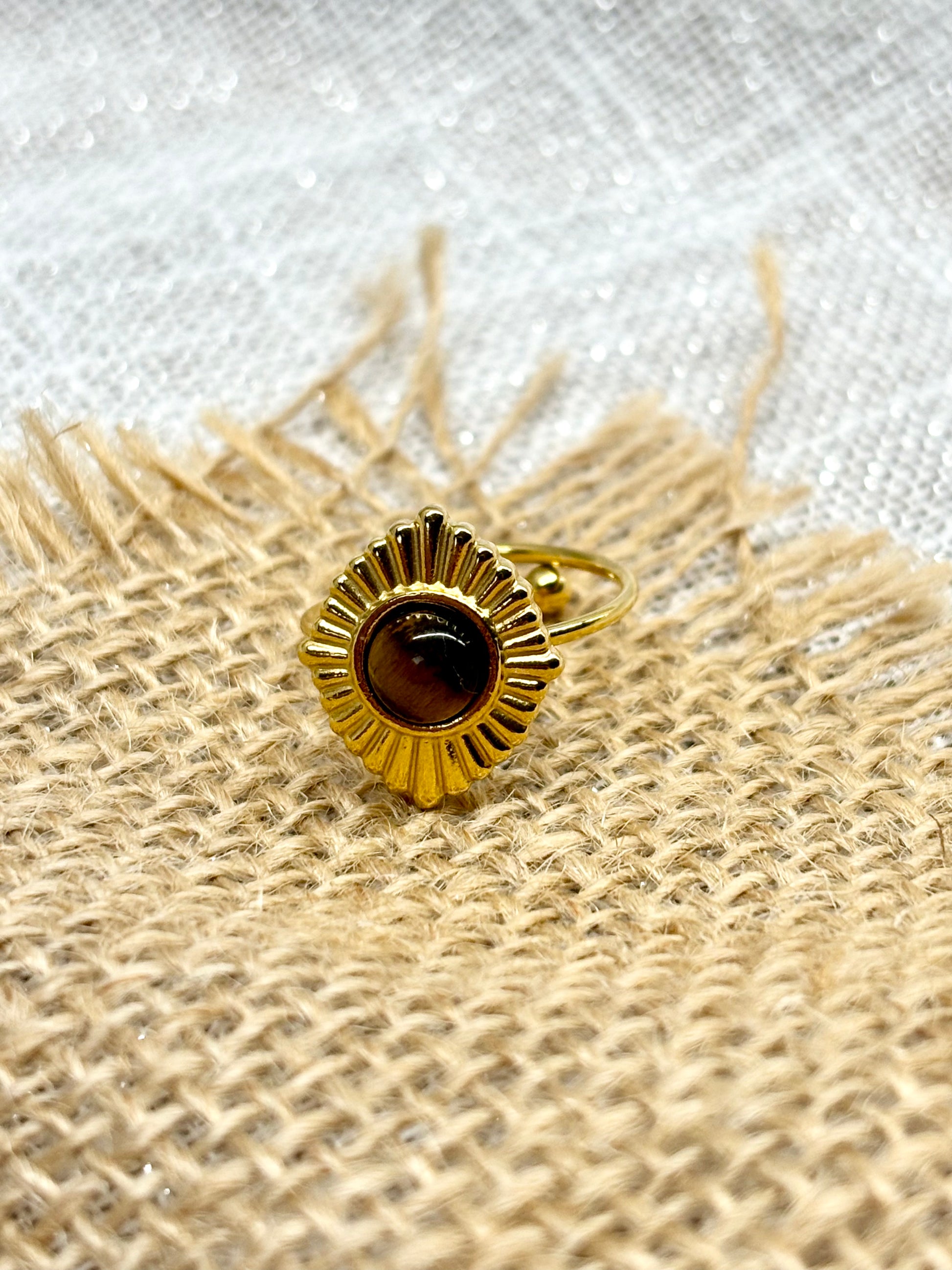 Bague ALYSÉE, de couleur dorée avec pierre d'Oeil de Tigre, exposée sur un fond en lin et toile de jute.