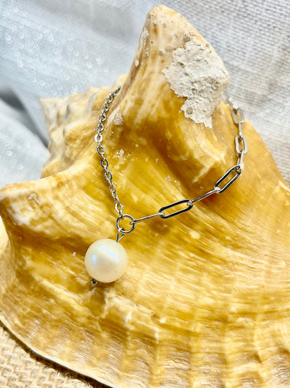 Collier ANGÈLE, de couleur argent avec Perle de Culture, exposé sur un coquillage.