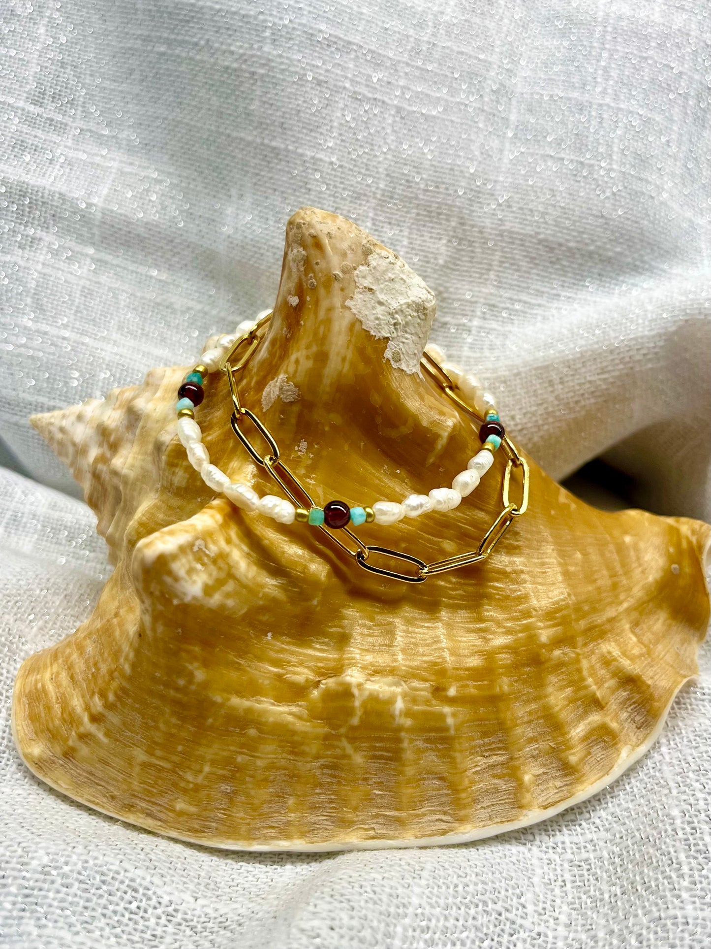 Bracelet ARIANA, avec pierre d'Amazonite, de Grenat et Perle de Culture, exposé sur un coquillage.