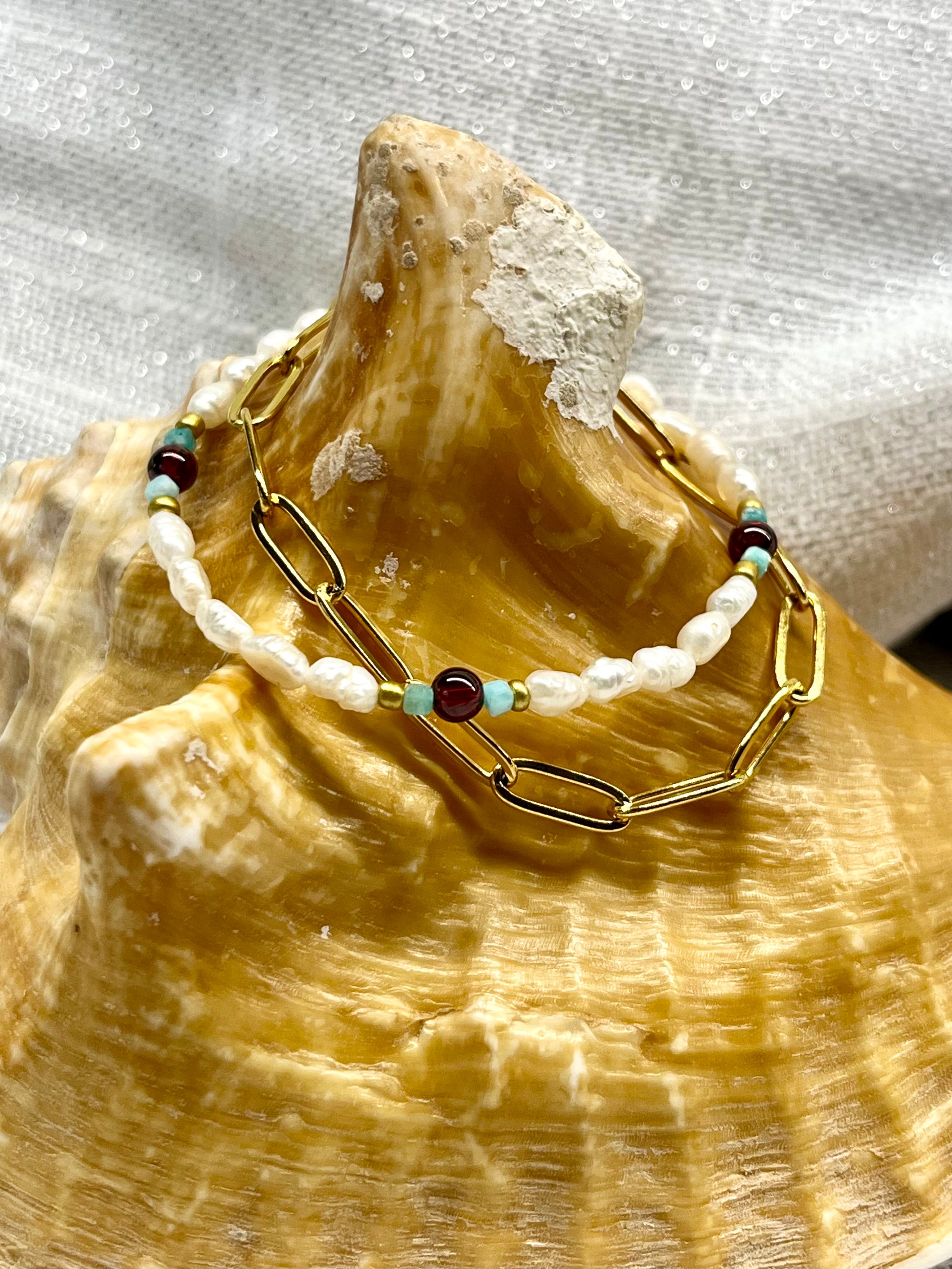 Bracelet ARIANA, avec pierre d'Amazonite, de Grenat et Perle de Culture, exposé sur un coquillage.