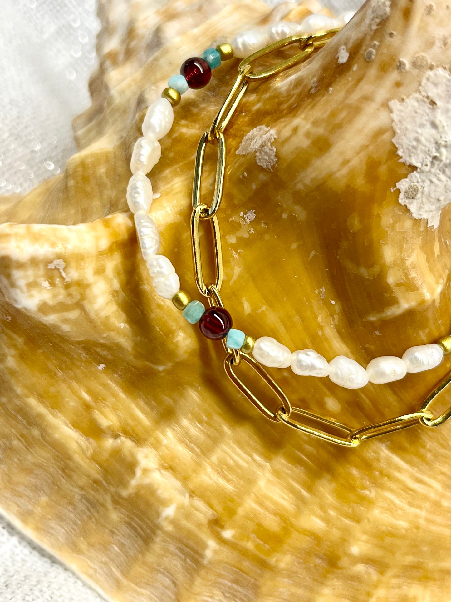 Bracelet ARIANA, avec pierre d'Amazonite, de Grenat et Perle de Culture, exposé sur un coquillage.