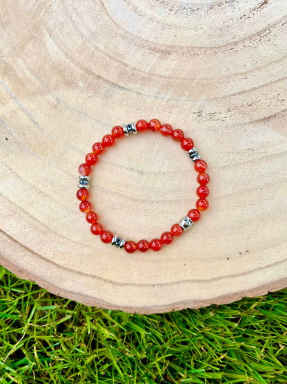 Bracelet CAMILLE, avec pierres de Cornaline et d'Hématite, exposé sur un rondin de bois.
