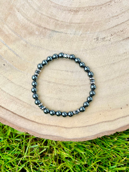 Bracelet CAMILLE, avec pierres d'Hématite, exposé sur un rondin de bois.