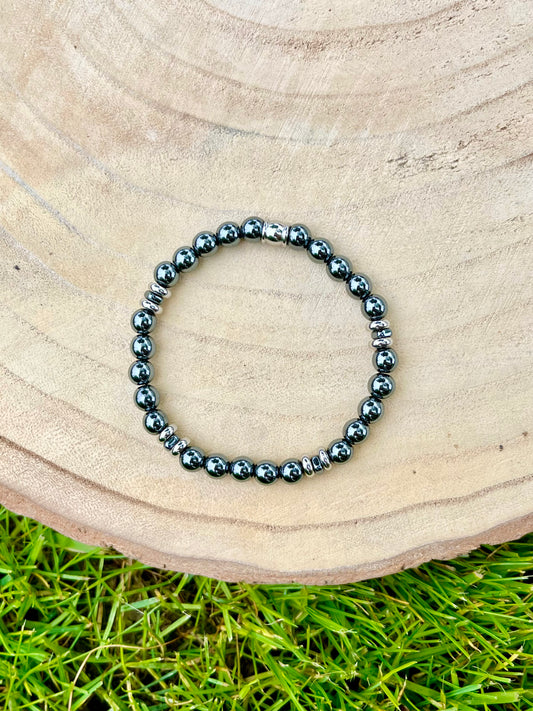 Bracelet CAMILLE, avec pierres d'Hématite, exposé sur un rondin de bois.