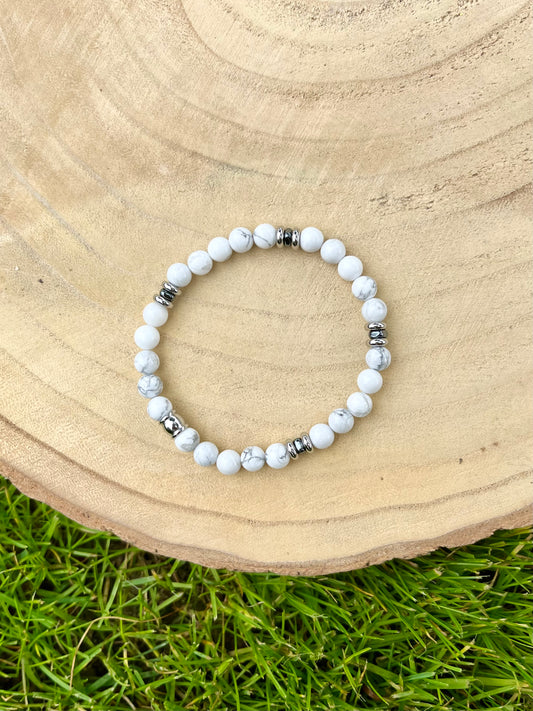 Bracelet CAMILLE, avec pierres d'Howlite et d'Hématite, exposé sur un rondin de bois.