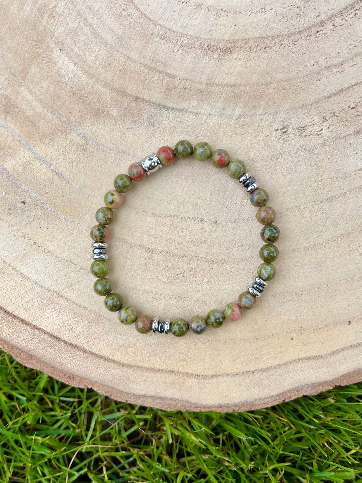 Bracelet CAMILLE, avec pierres d'Unakite et d'Hématite, exposé sur un rondin de bois.