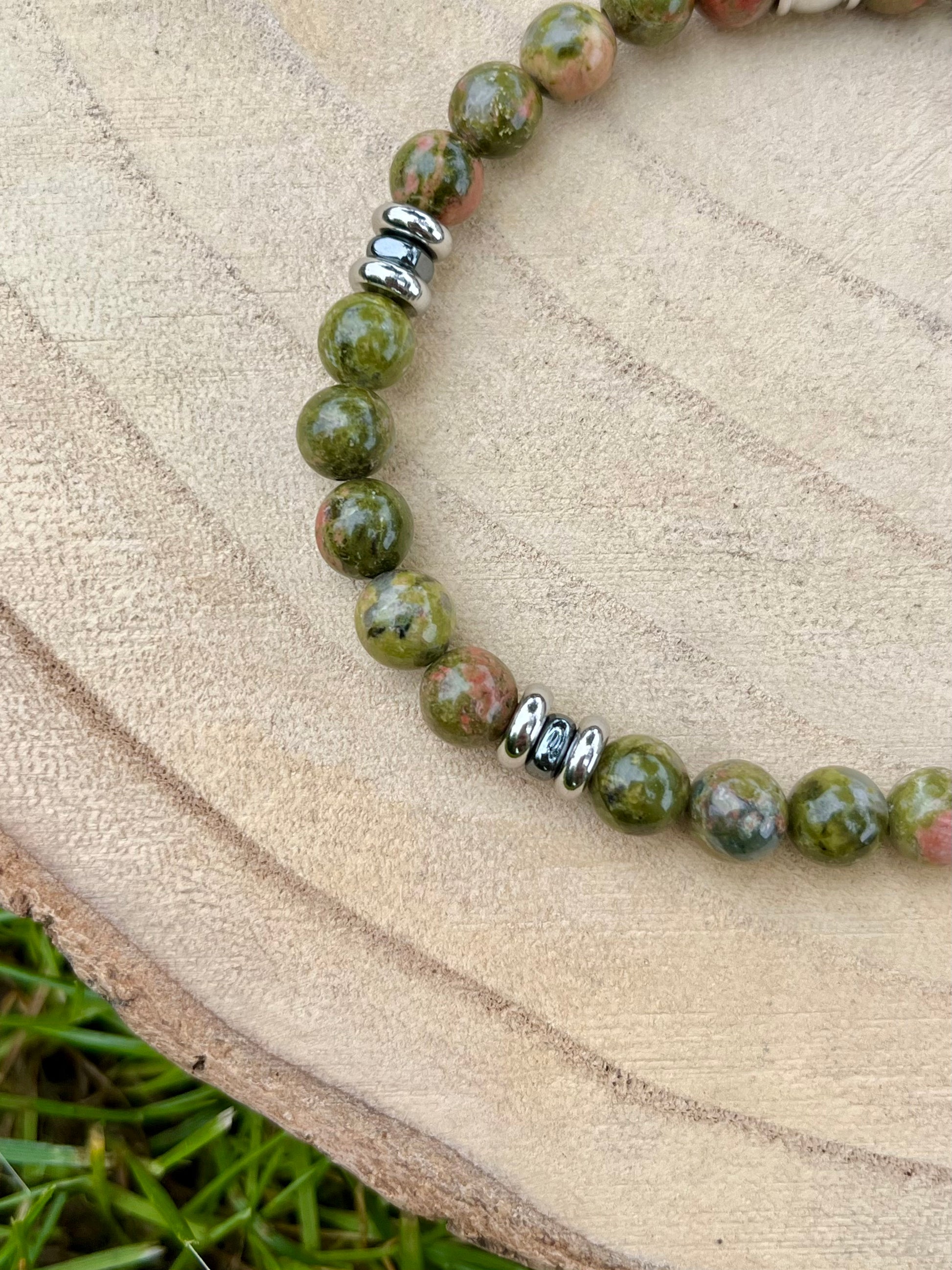 Bracelet CAMILLE, avec pierres d'Unakite et d'Hématite, exposé sur un rondin de bois.