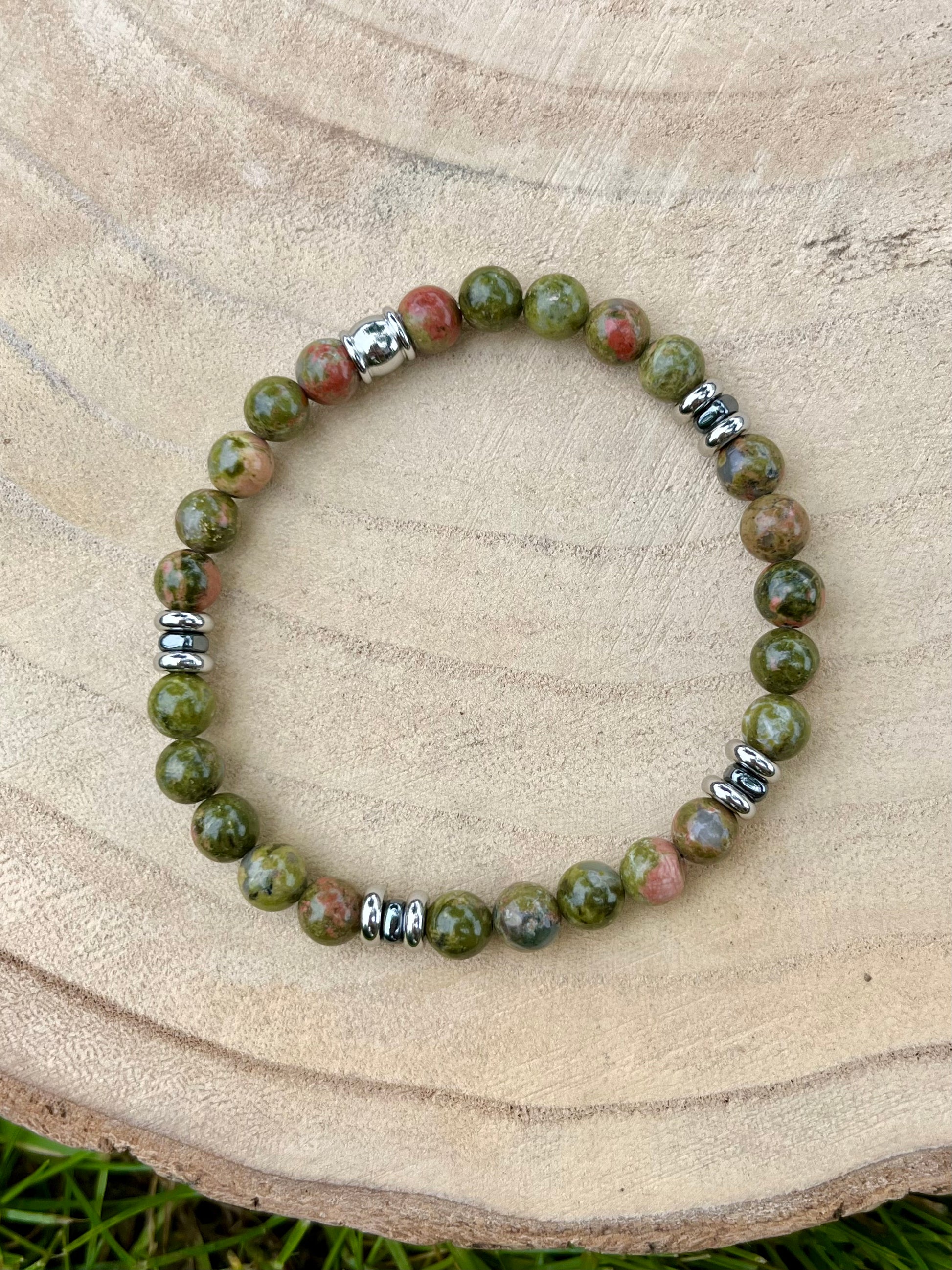Bracelet CAMILLE, avec pierres d'Unakite et d'Hématite, exposé sur un rondin de bois.
