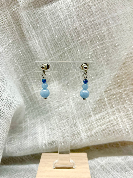 Boucles d'oreille EMMA, avec pierres d'Angélite et de Saphir, exposées devant un fond en lin.