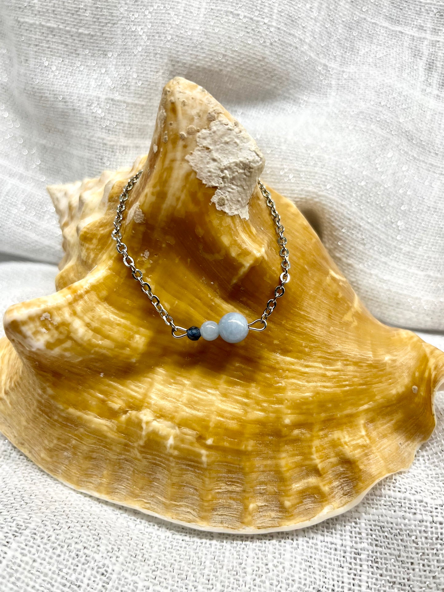Bracelet EMMA, avec pierres d'Angélite et de Saphir, exposé sur un coquillage.