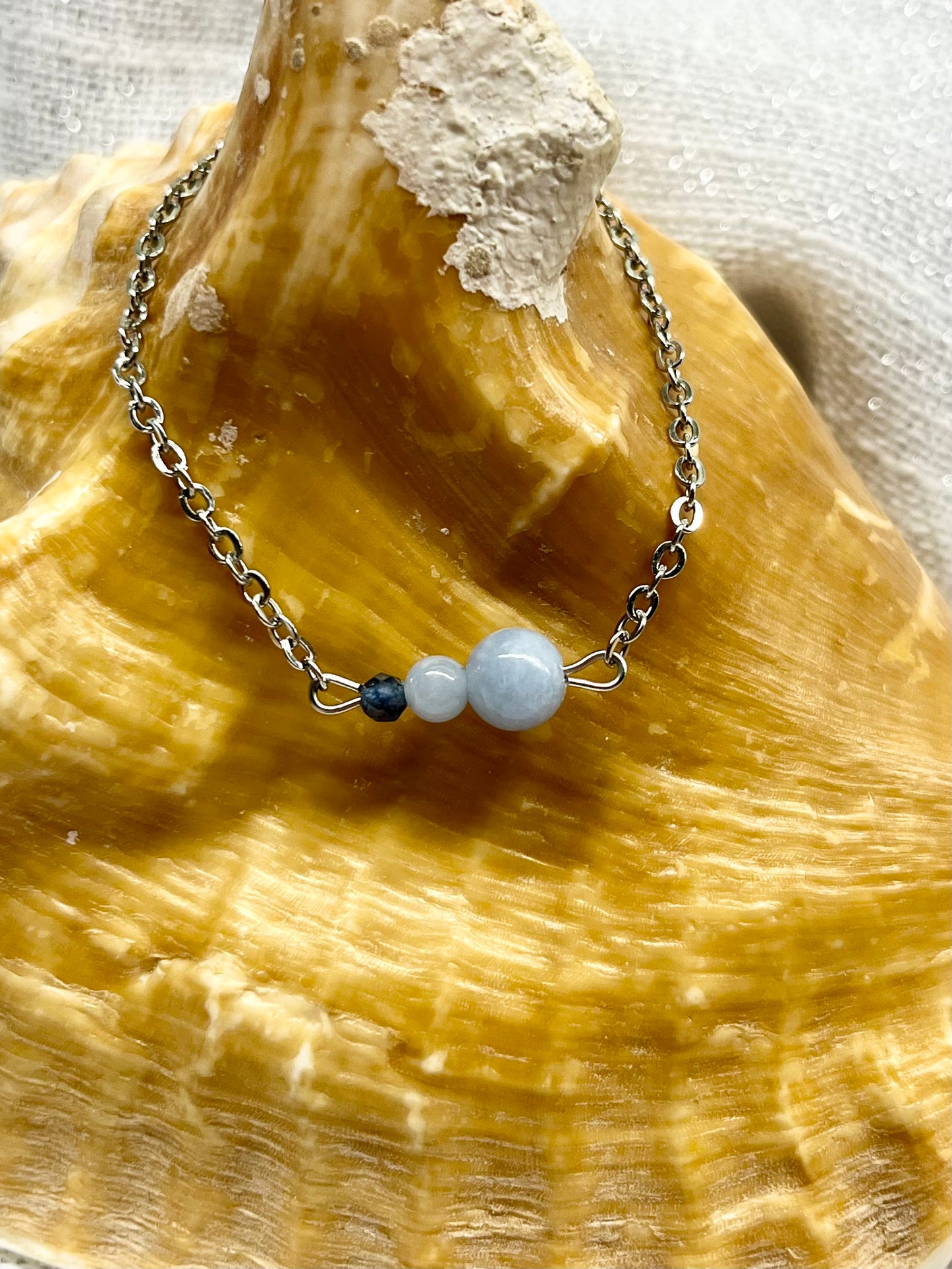 Bracelet EMMA, avec pierres d'Angélite et de Saphir, exposé sur un coquillage.