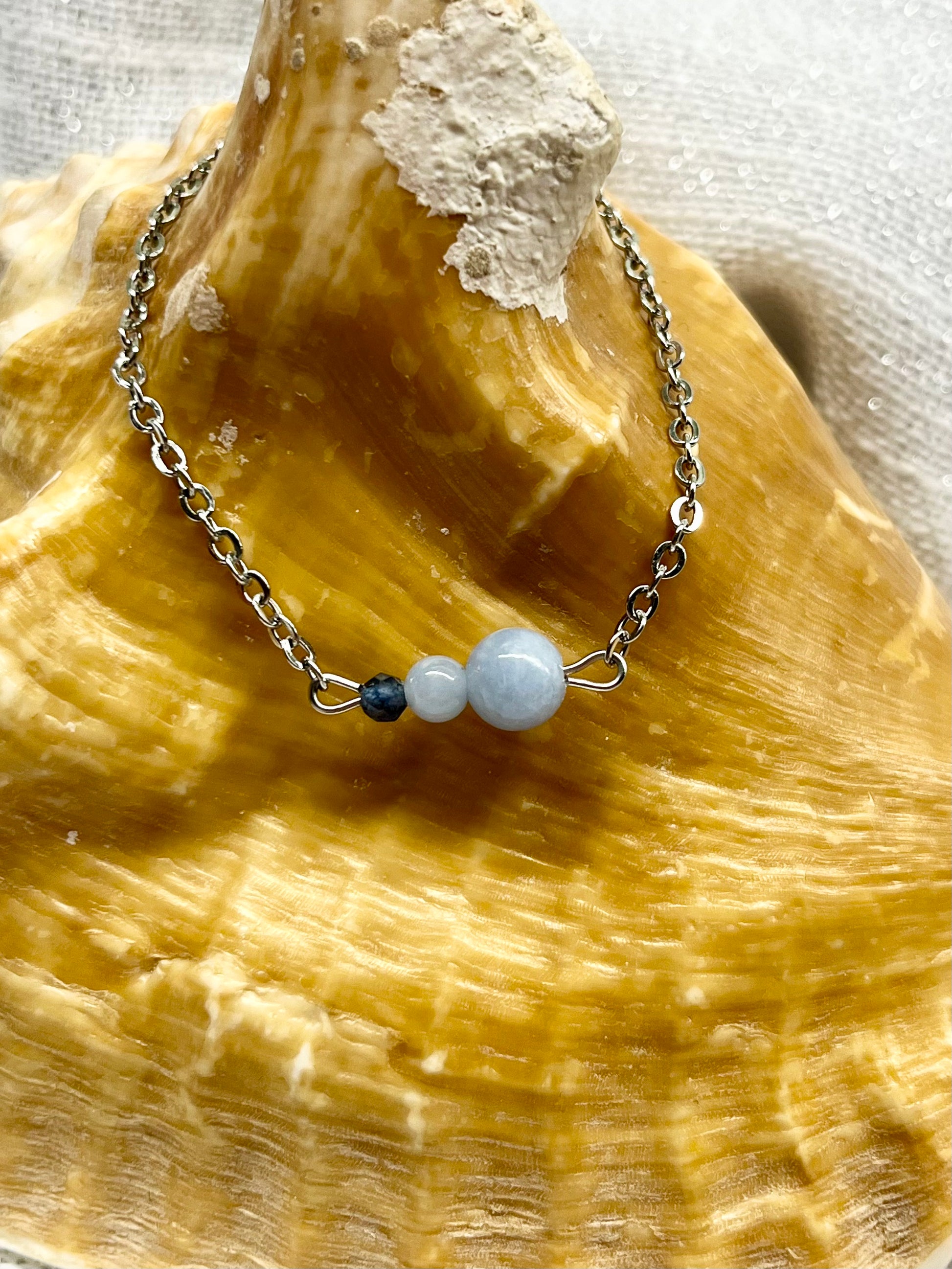 Bracelet EMMA, avec pierres d'Angélite et de Saphir, exposé sur un coquillage.