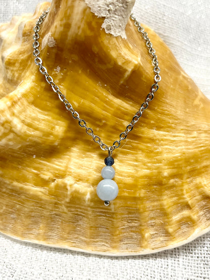 Collier EMMA, avec pierres d'Angélite et de Saphir, exposé sur un coquillage.