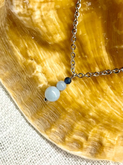 Collier EMMA, avec pierres d'Angélite et de Saphir, exposé sur un coquillage.
