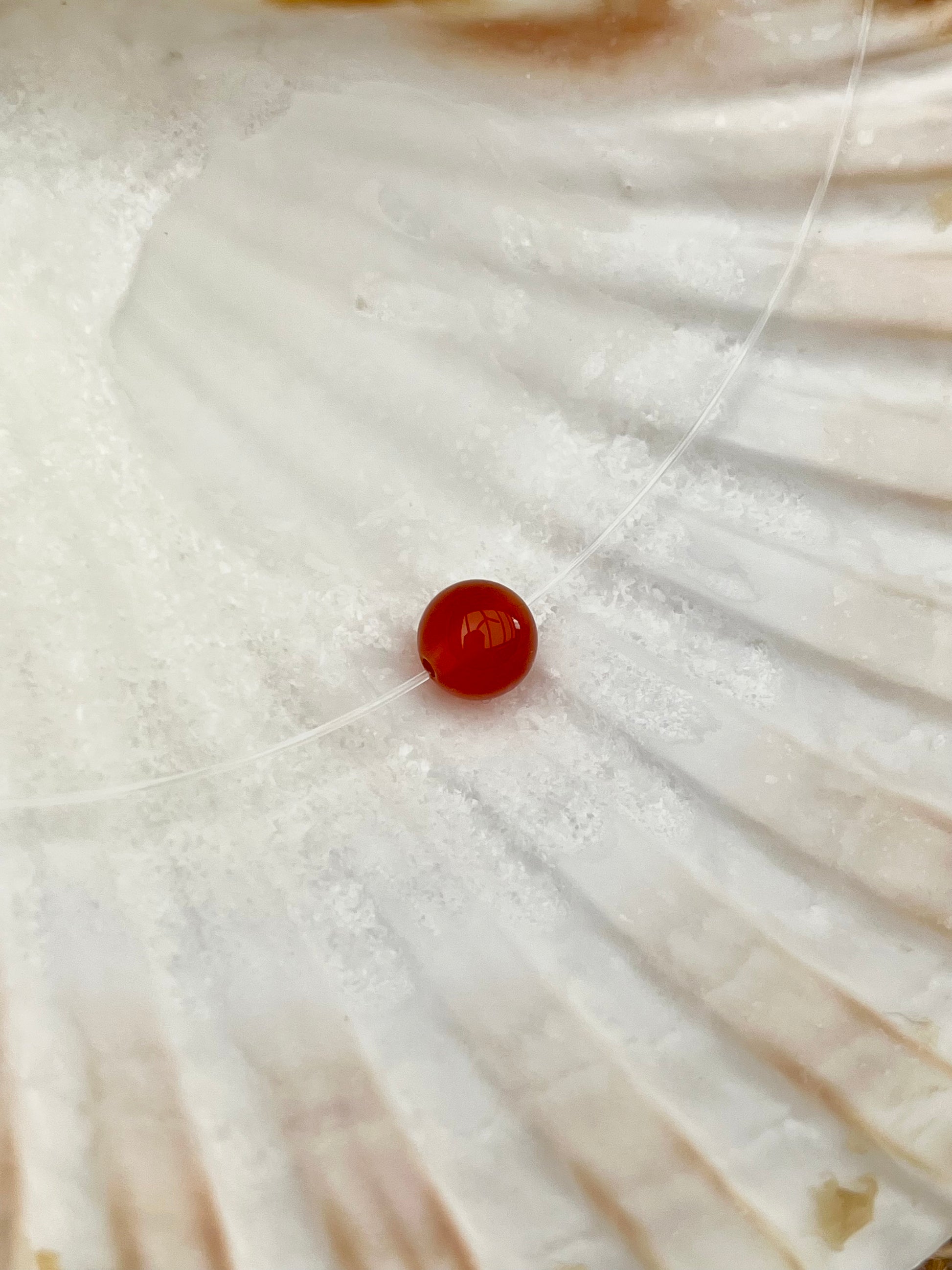 Collier EMY, avec pierre de Cornaline, exposé dans un coquillage.