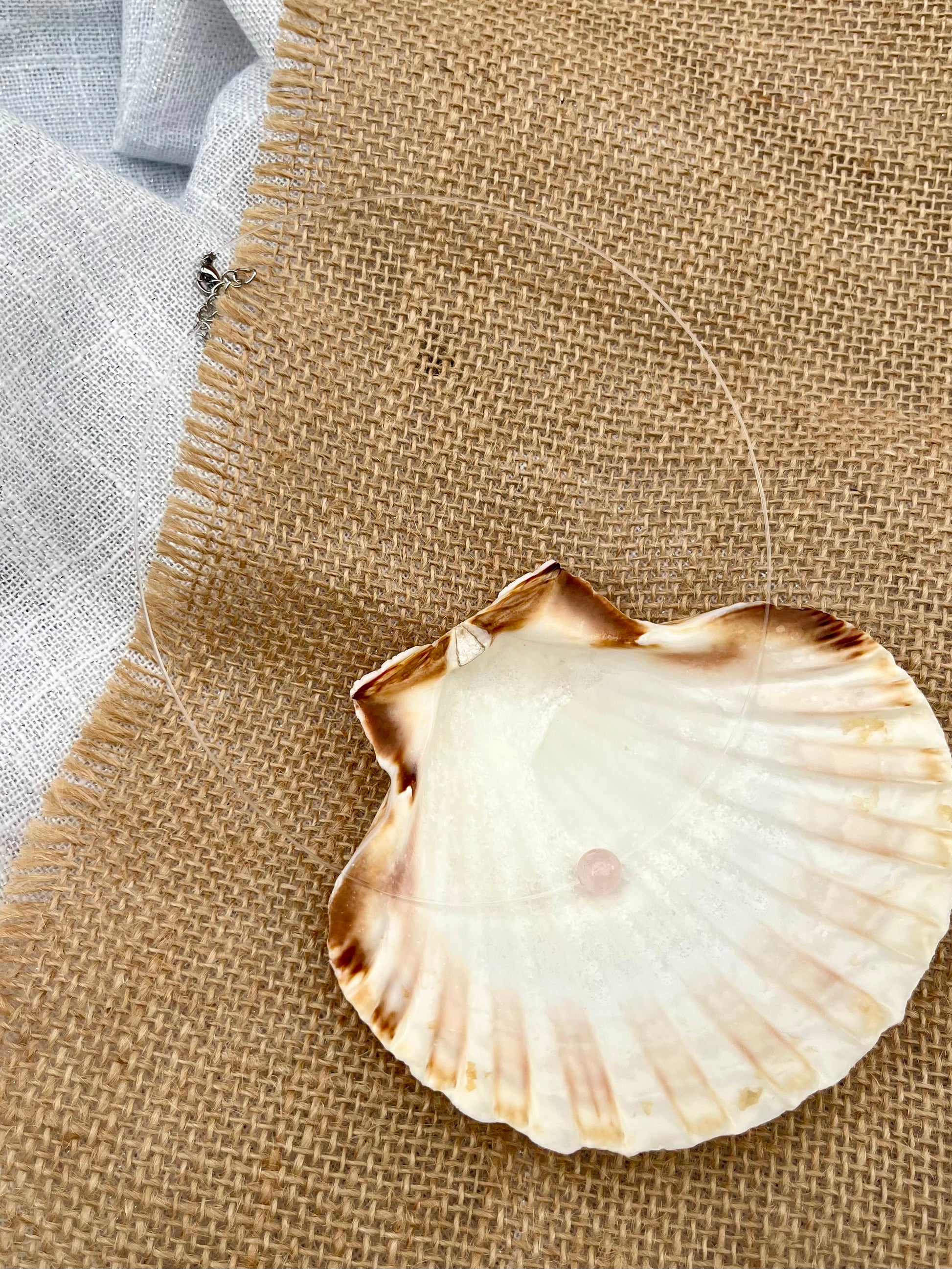 Collier EMY, avec pierre de Quartz Rose, exposé dans un coquillage.