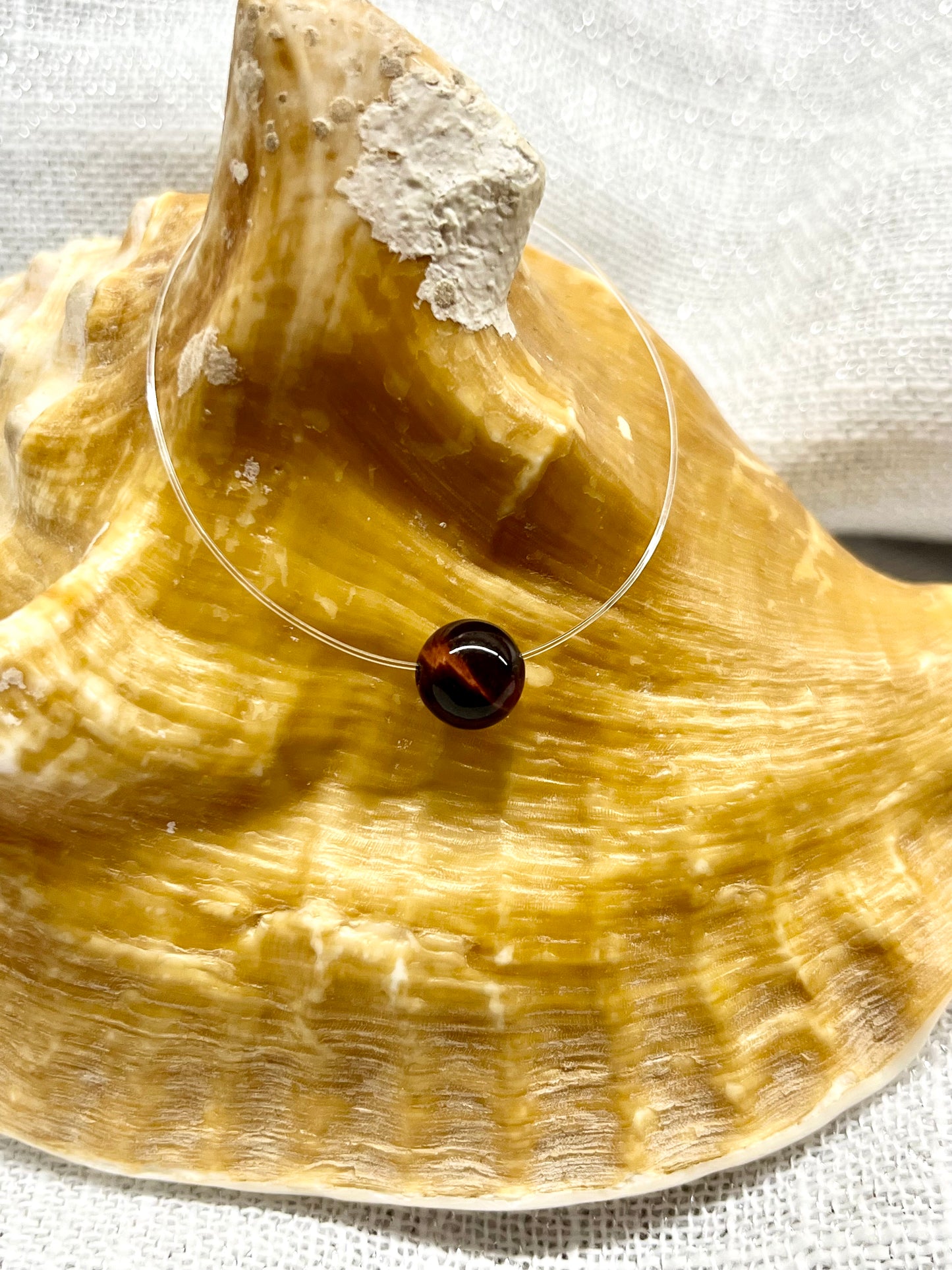Collier EMY avec pierre d'Oeil de Taureau, exposé sur un coquillage.