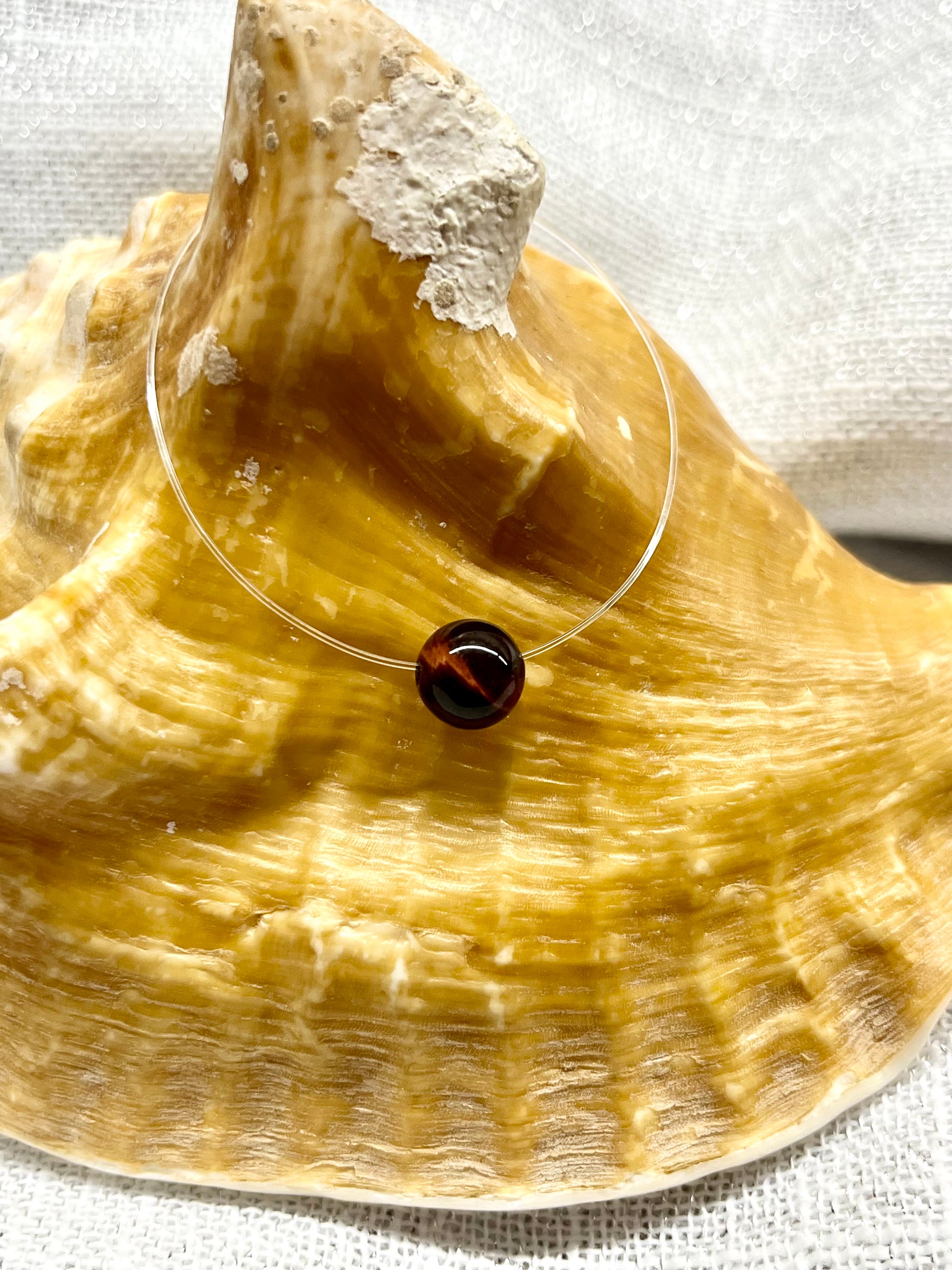 Collier EMY avec pierre d'Oeil de Taureau, exposé sur un coquillage.