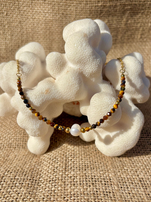 Collier doré ÈVE en Œil de Tigre et perle de culture, présenté sur un corail blanc naturel.