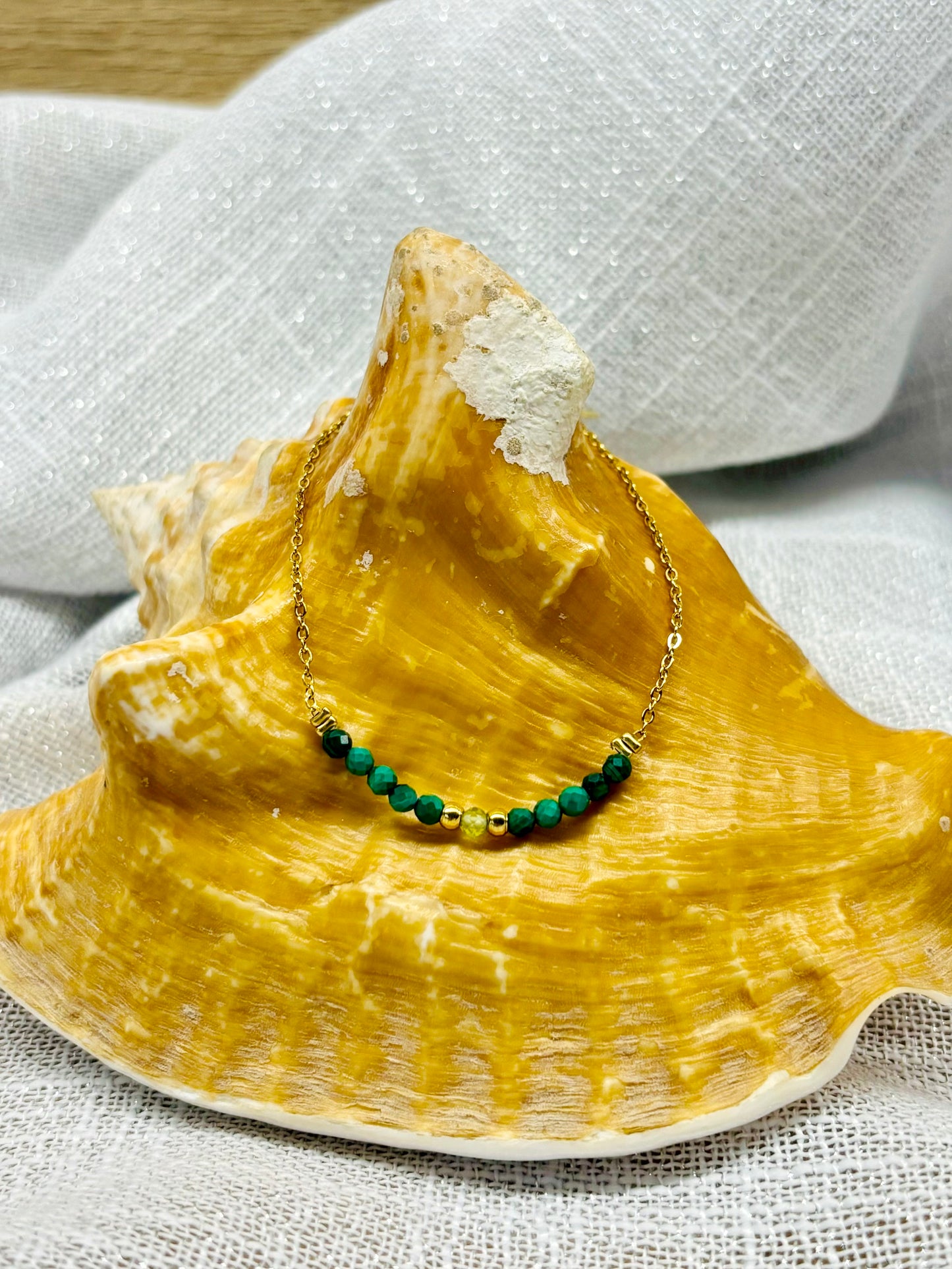 Collier JULIE, avec pierres de Malachite et de Péridot, exposé sur un coquillage.