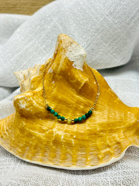 Collier JULIE, avec pierres de Malachite et de Péridot, exposé sur un coquillage.