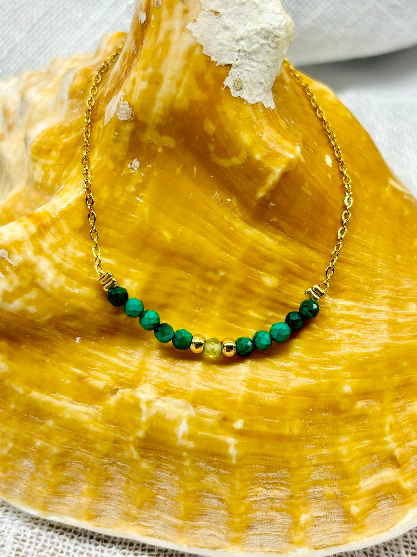 Collier JULIE, avec pierres de Malachite et de Péridot, exposé sur un coquillage.