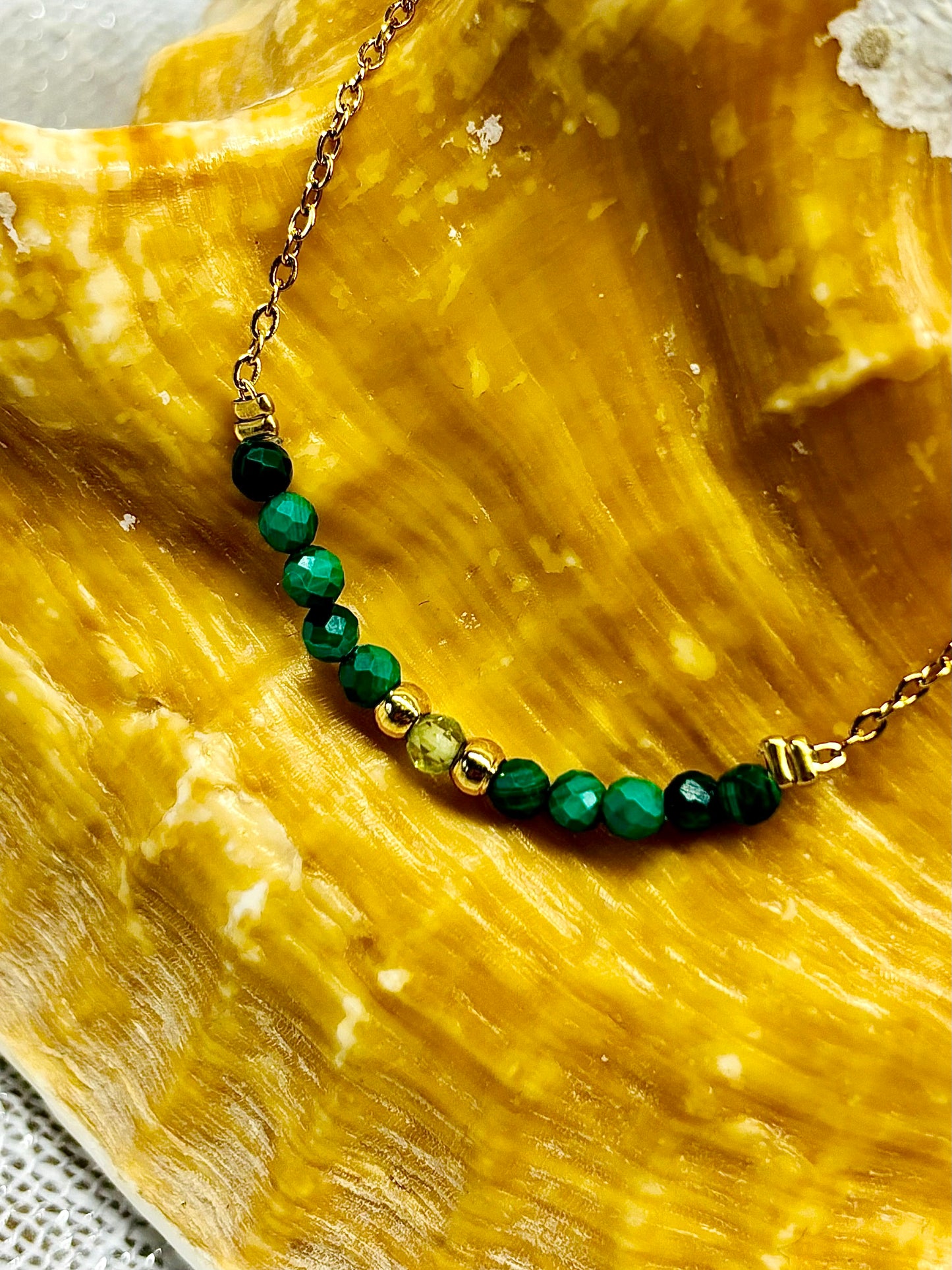 Collier JULIE, avec pierres de Malachite et de Péridot, exposé sur un coquillage.