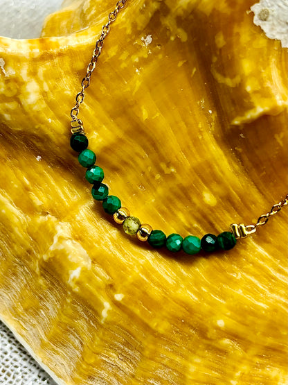 Collier JULIE, avec pierres de Malachite et de Péridot, exposé sur un coquillage.