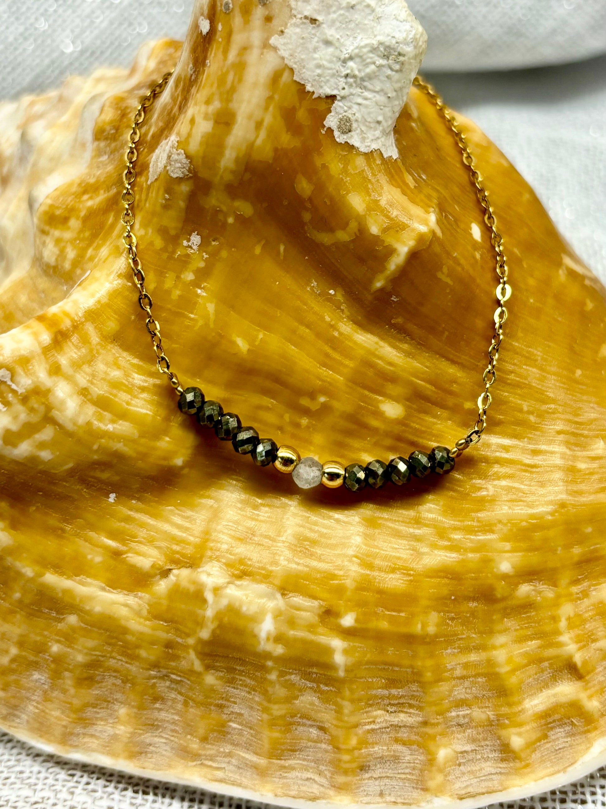 Collier JULIE, avec pierres de Pyrite et de Labradorite, exposé sur un coquillage.