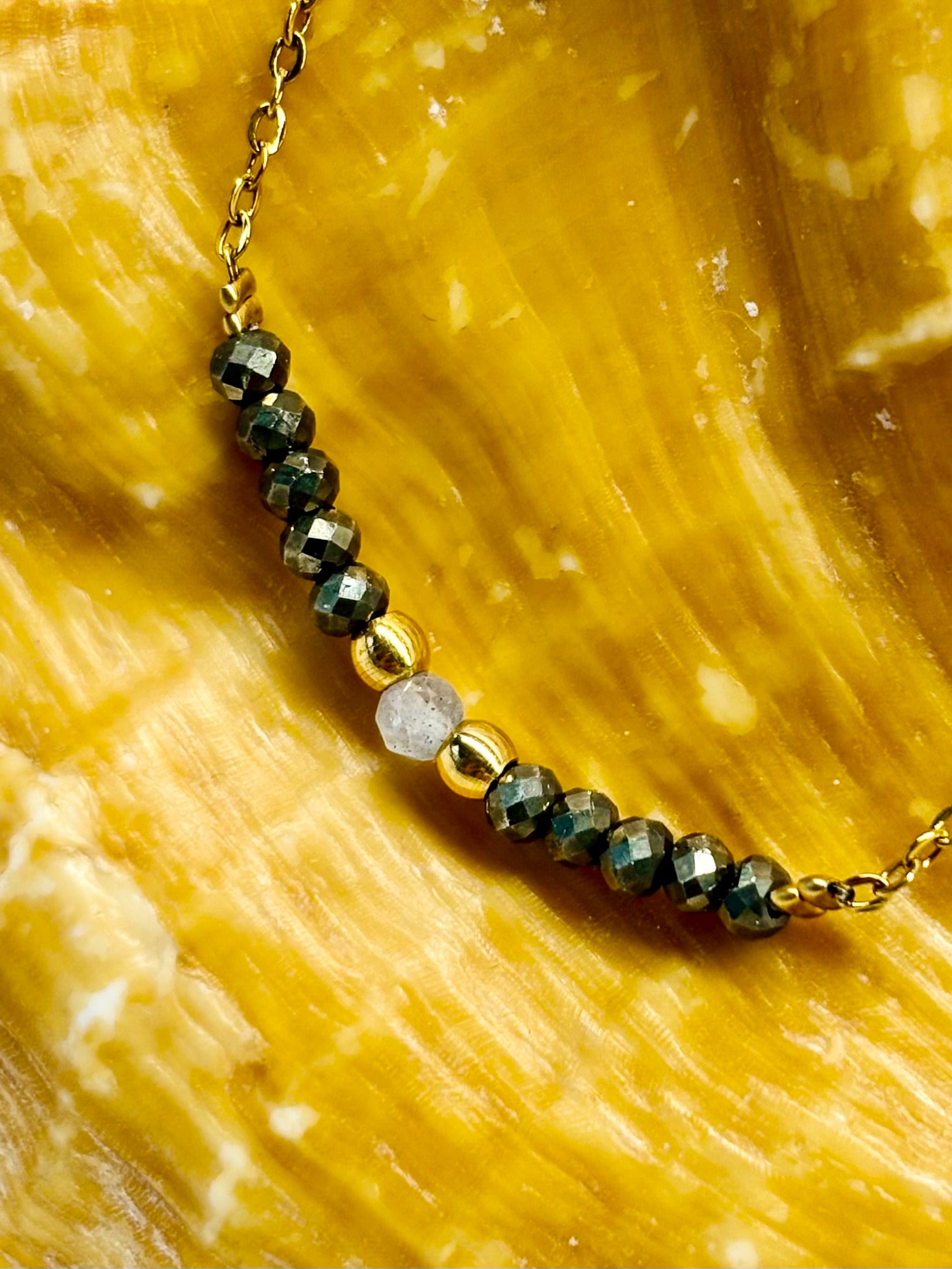 Collier JULIE, avec pierres de Pyrite et de Labradorite, exposé sur un coquillage.