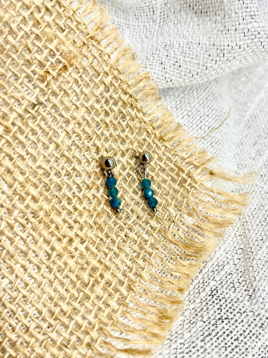 Boucles d'oreille LALY, avec pierre d'Apatite, exposées sur un fond en toile de jute.
