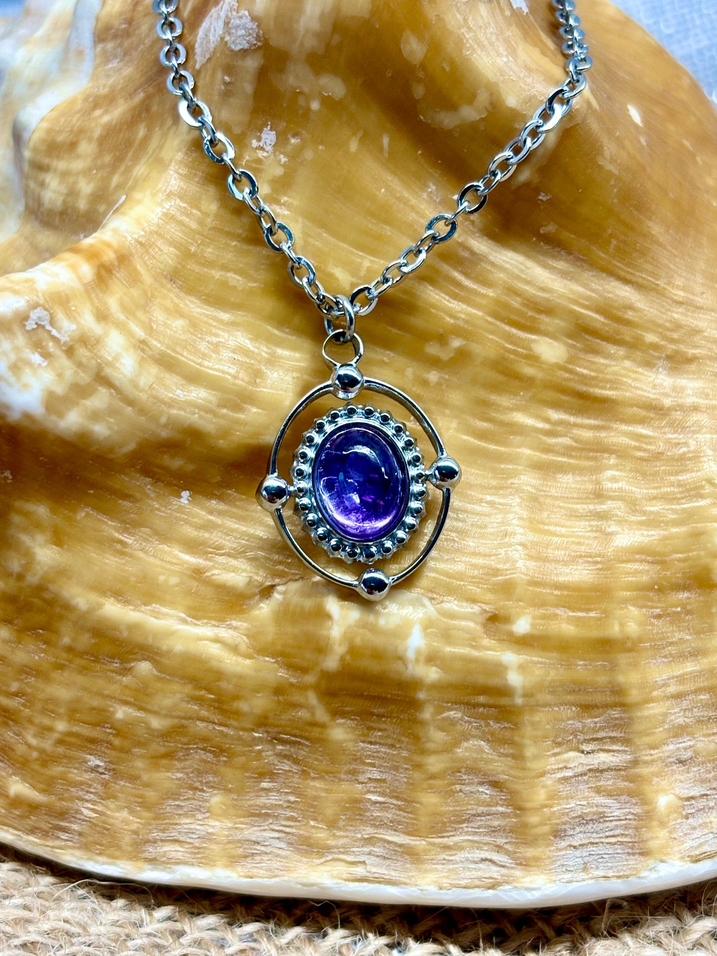 Collier LOUISA, de couleur argent avec pierre d'Améthyste, exposé sur un coquillage.