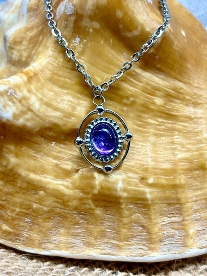 Collier LOUISA, de couleur argent avec pierre d'Améthyste, exposé sur un coquillage.
