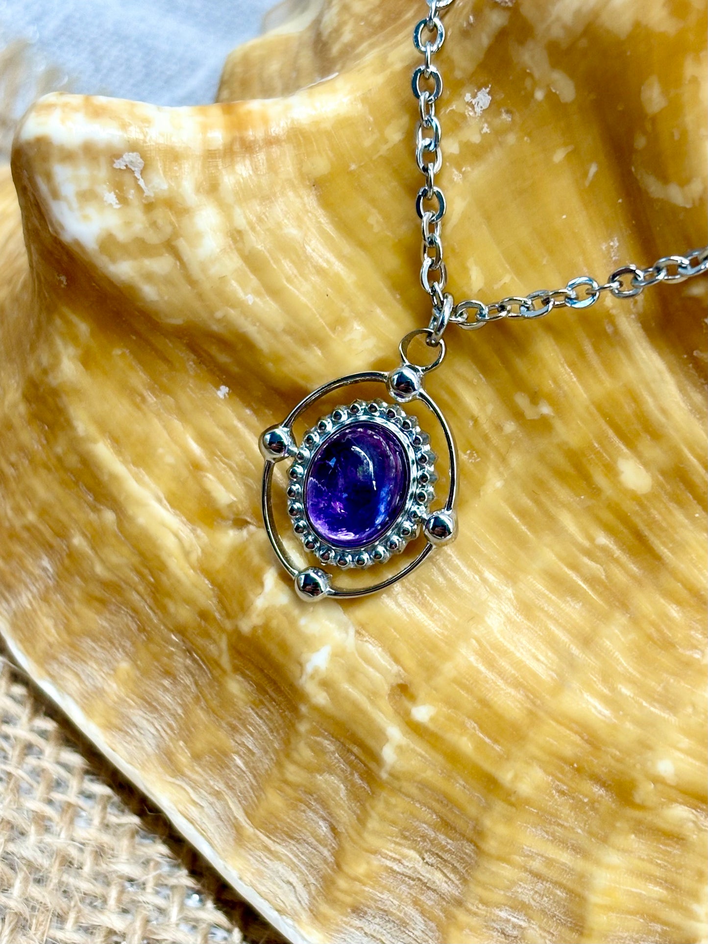Collier LOUISA, de couleur argent avec pierre d'Améthyste, exposé sur un coquillage.