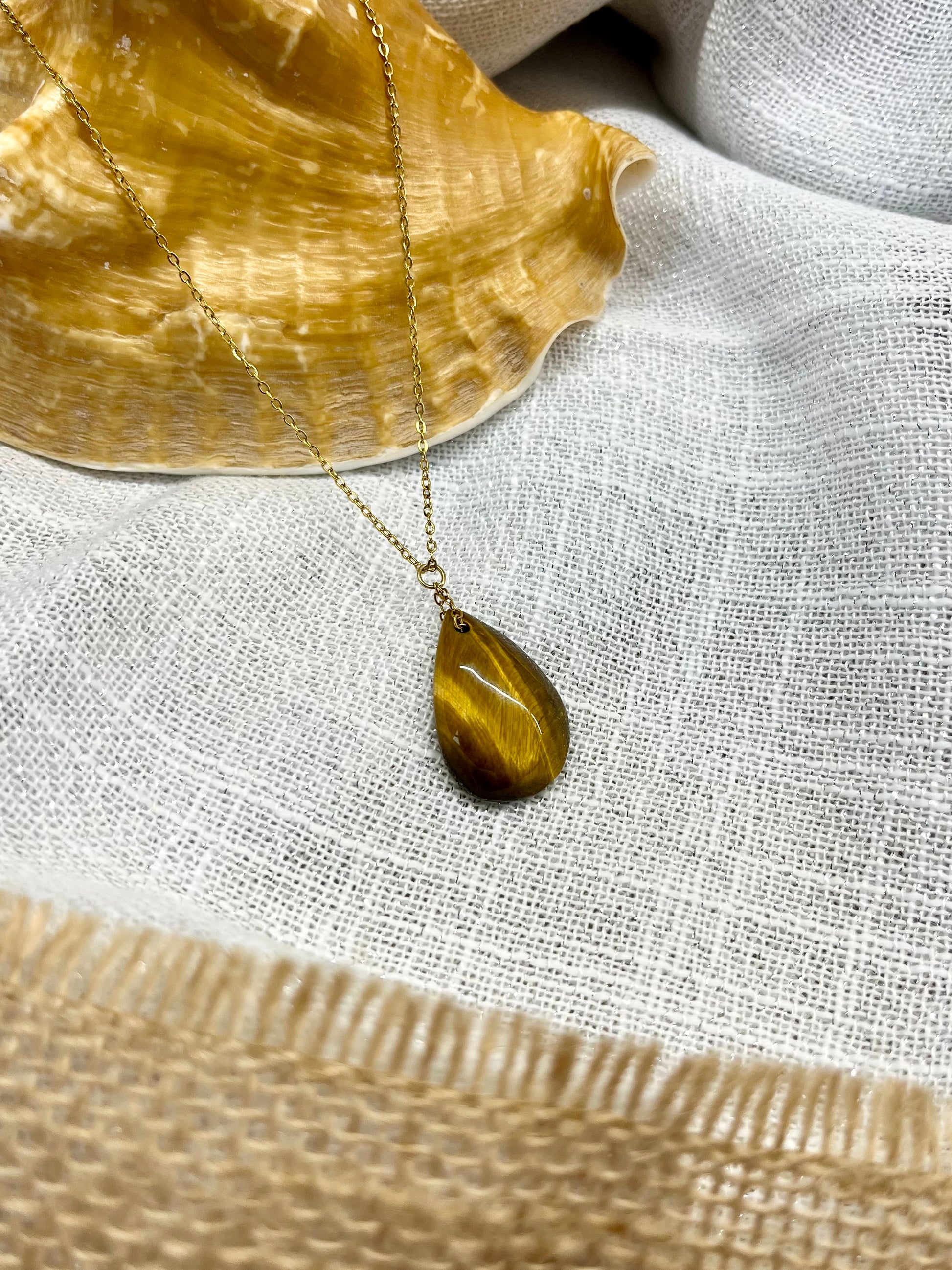 Collier MAELA, avec pierre d'Oeil de Tigre, exposé sur un fond en lin.