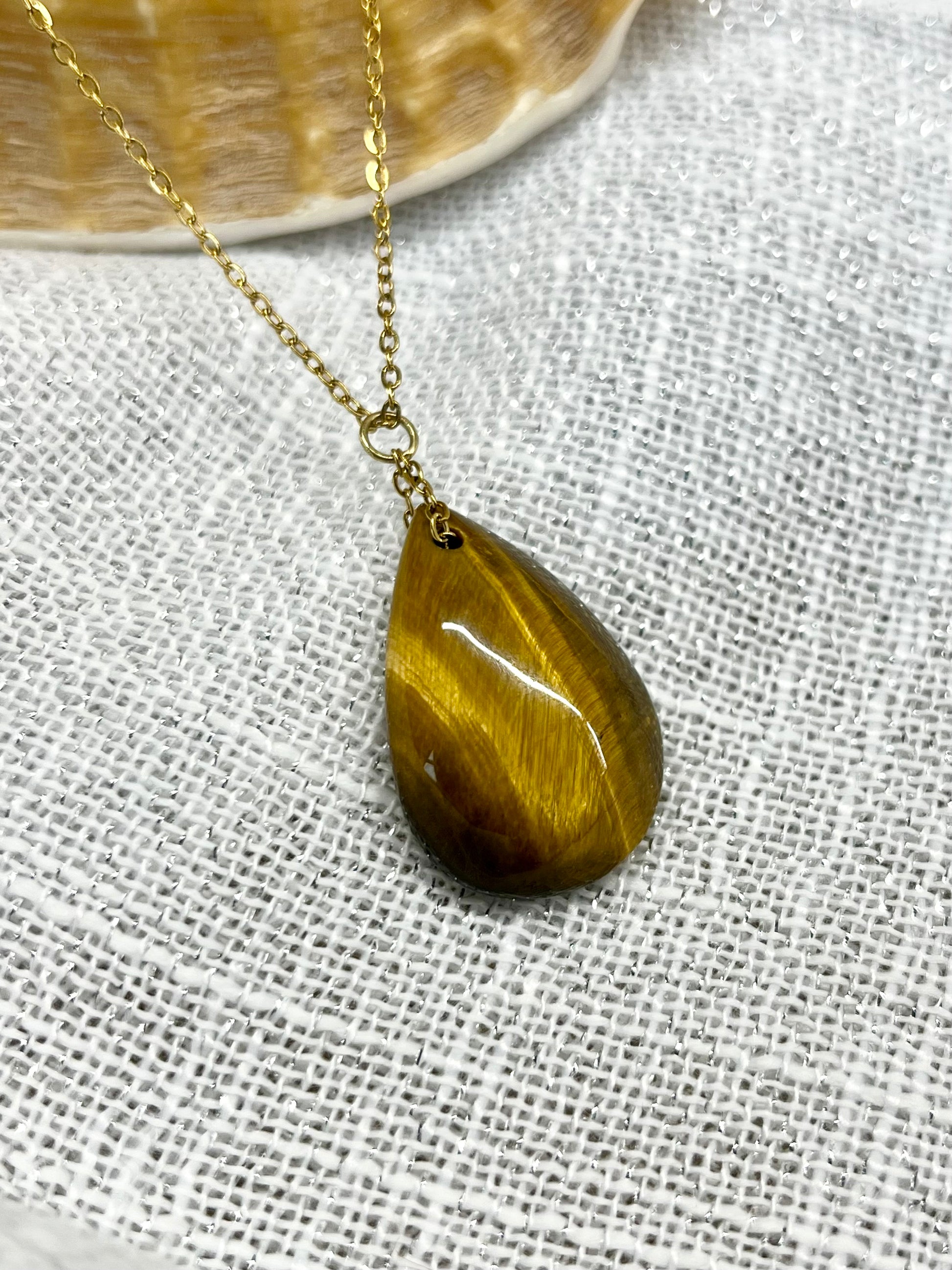 Collier MAELA, avec pierre d'Oeil de Tigre, exposé sur un fond en lin.