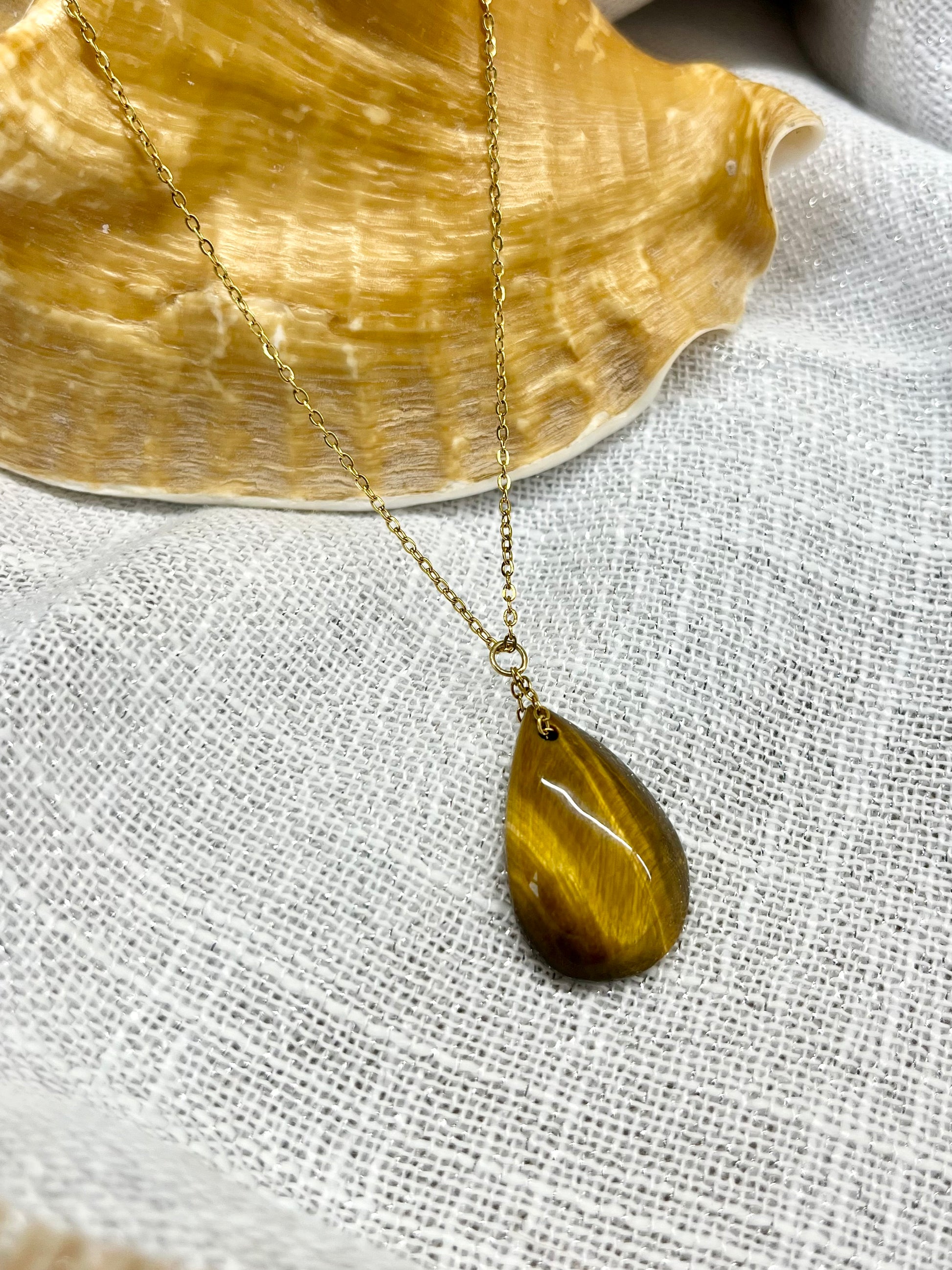 Collier MAELA, avec pierre d'Oeil de Tigre, exposé sur un fond en lin.