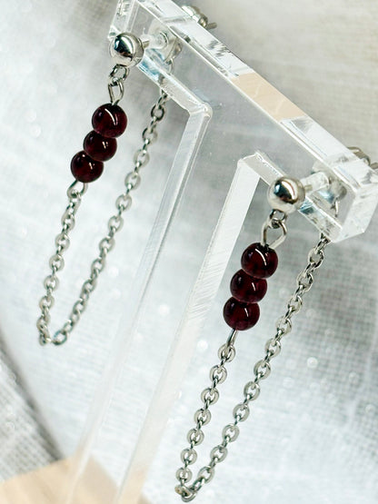 Boucles d'oreille MALIA, de couleur argent, exposées devant un fond en lin.