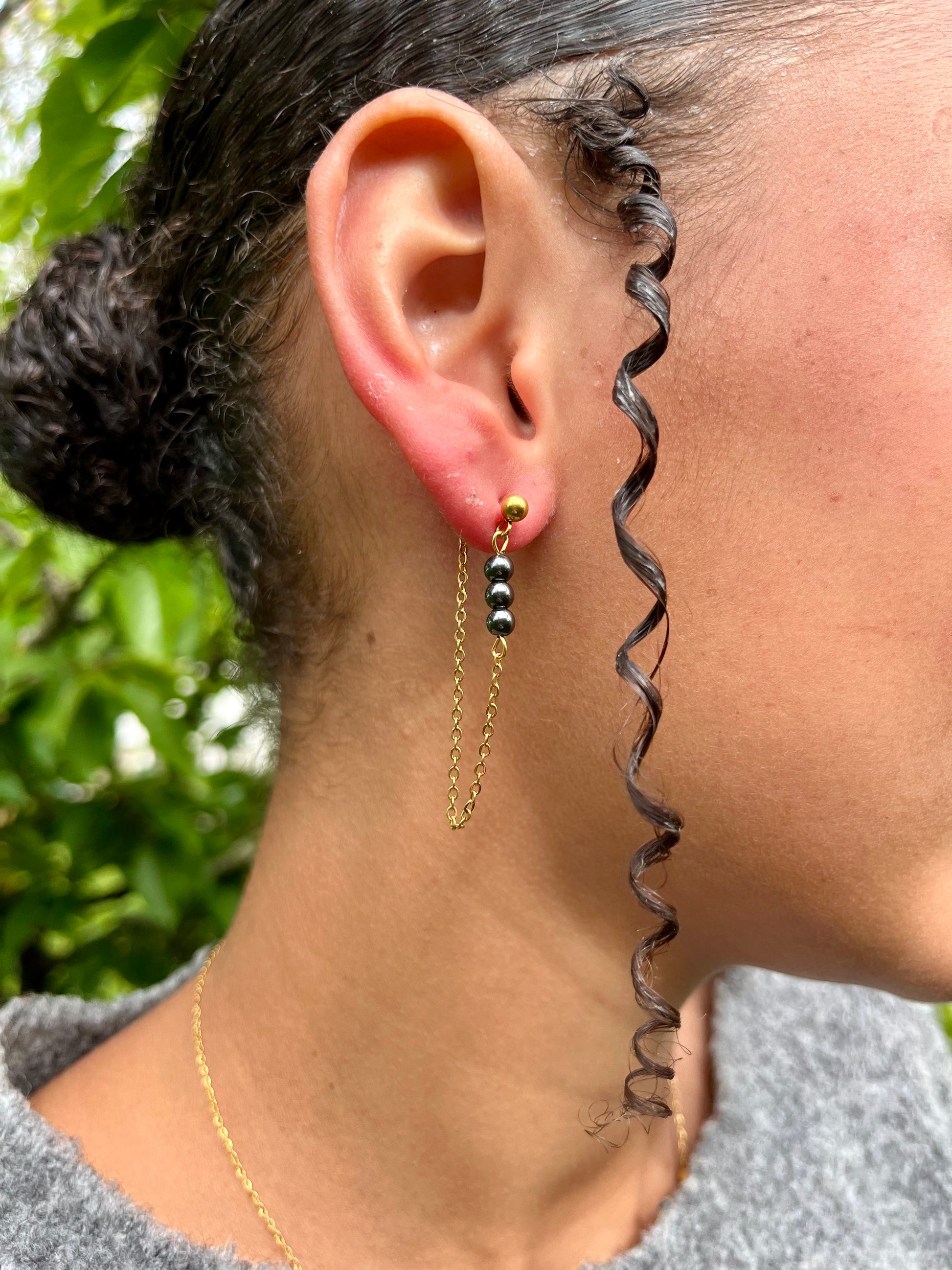 Boucles d'oreille MALIA, de couleur dorée avec pierres d'hématite, portées.