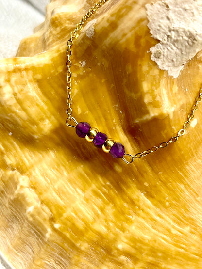 Bracelet MALIA, de couleur doré avec pierres d'Améthyste, exposé sur un coquillage.