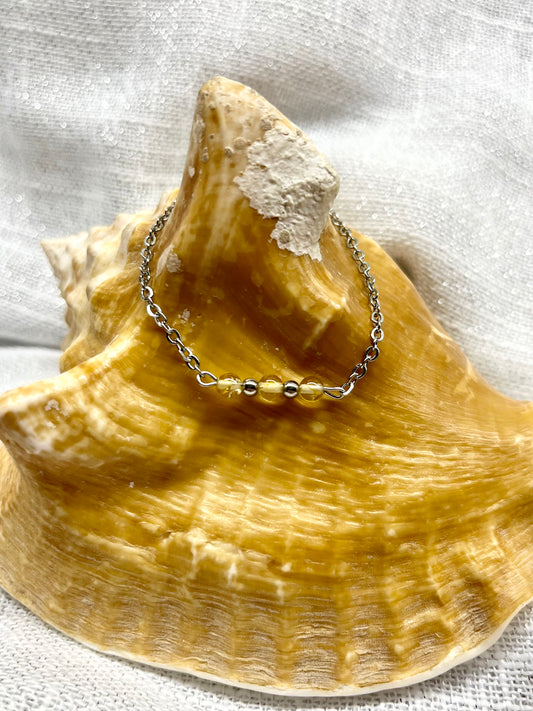 Bracelet MALIA, de couleur argent avec pierres de Citrine, exposé sur un coquillage.