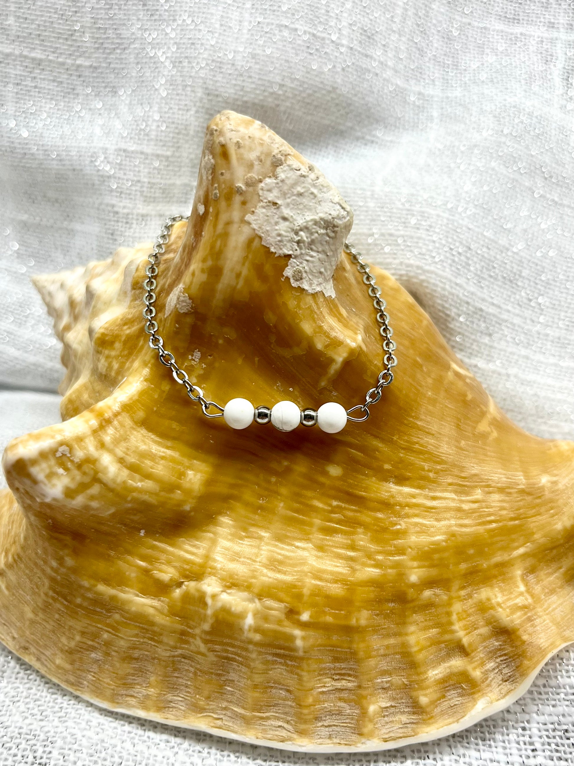 Bracelet MALIA, de couleur argent avec pierres d'Howlite, exposé sur un coquillage.