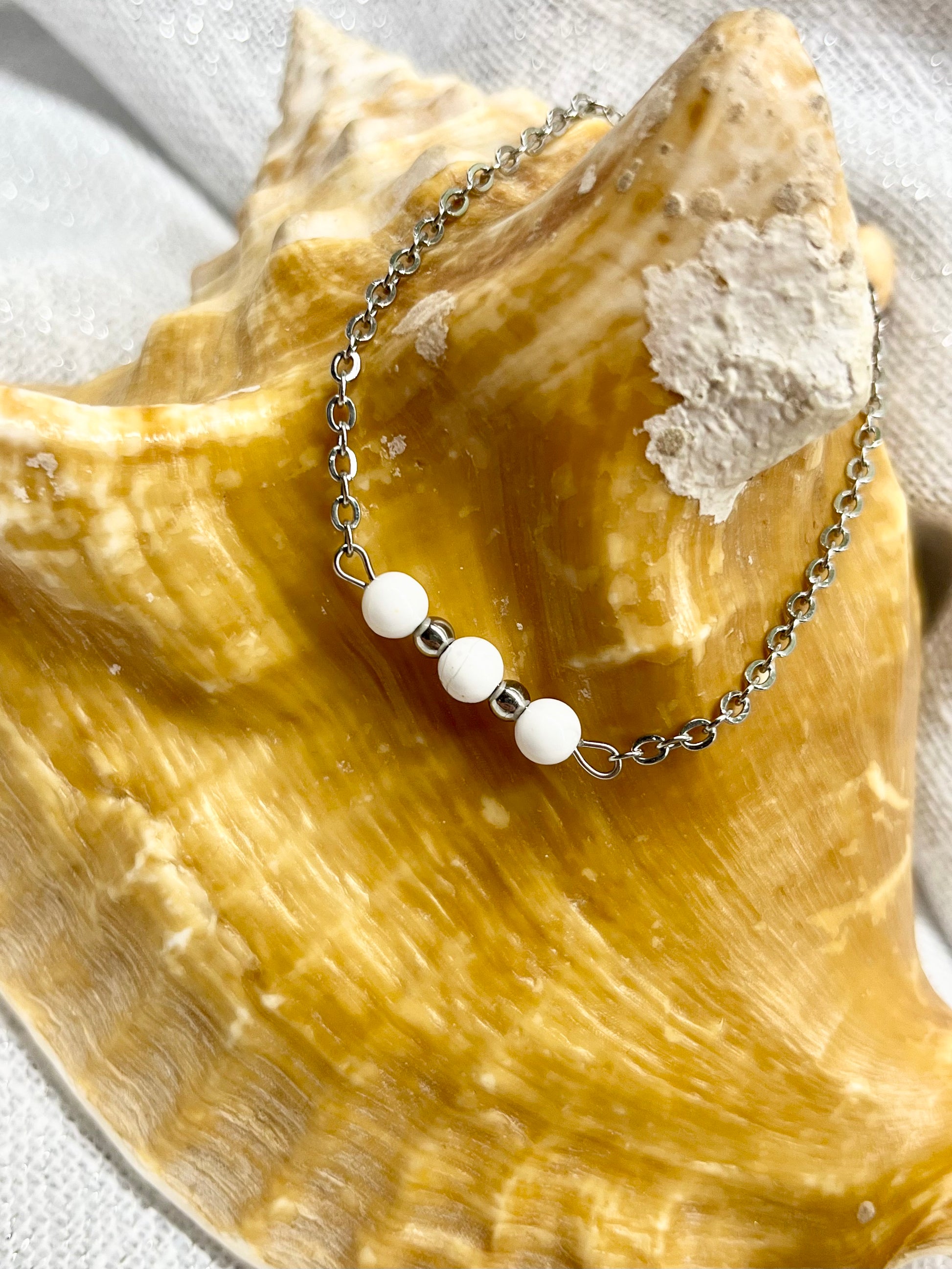 Bracelet MALIA, de couleur argent avec pierres d'Howlite, exposé sur un coquillage.